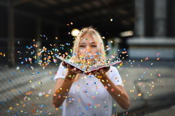 Bild på en tjej som håller i en bok som hon blåser konfetti ifrån
