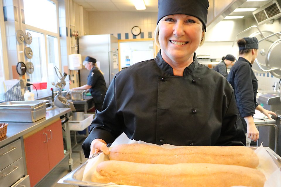 Kommundirektör Karina Hansson bär en plåt med nybakat bröd, i Sandbäcksskolans skolkök.