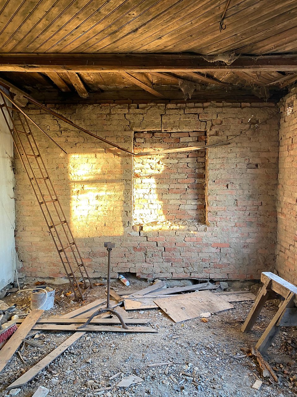 Solen lyser in i vardagsrummet utan golv och mot väggen står en gammal rostig stege.