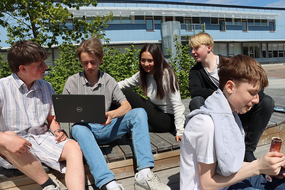 Fyra killar och en tjej sitter i solen på Färsingaskolans nya trädäck.