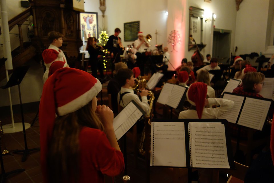 En bild från kulturskolans julkonsert, man ser barn med tomteluvor snett bakifrån som sitter i orkesterformering