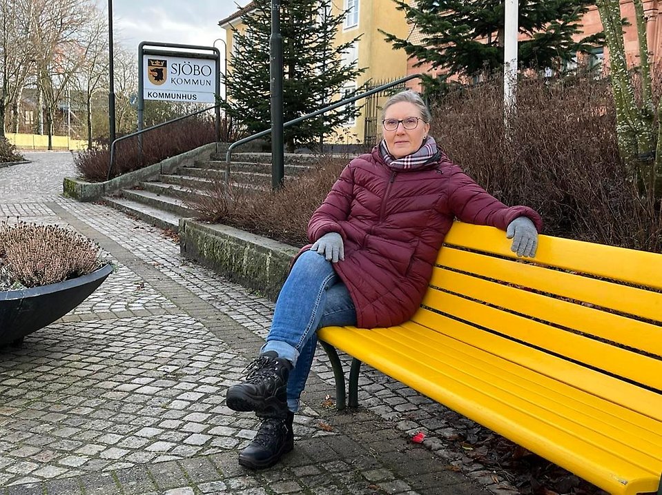 Bente sitter på vänskapsbänken framför kommunhuset